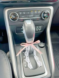 the interior of a car with an automatic gear lever and pink ribbon tied around it