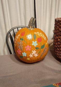 a painted pumpkin sitting on top of a table next to a wicker basket filled with flowers