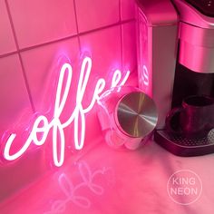 a pink neon sign that says coffee on the side of a wall next to a coffee maker