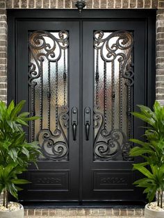 two potted plants sit in front of a black double door with intricate iron work