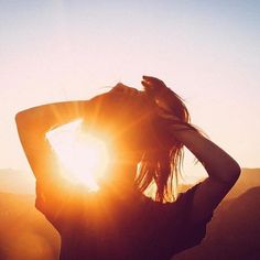 a woman standing in front of the sun with her hands on her head and arms behind her back