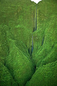 an aerial view of a waterfall surrounded by lush green hills