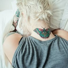 a woman laying in bed with her back turned to the camera and a butterfly tattoo on her neck