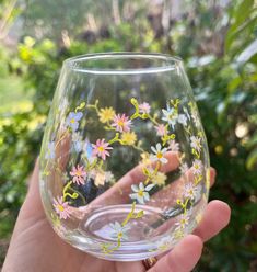 a hand holding up a wine glass with flowers painted on the outside and inside it