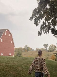 a person walking in the grass near a red barn