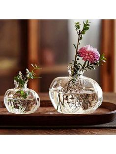 two clear vases with flowers in them on a wooden tray