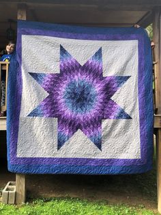 a purple and white quilt hanging from a wooden structure