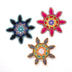 three embroidered appliques on white surface one is multicolored and the other has an abstract design