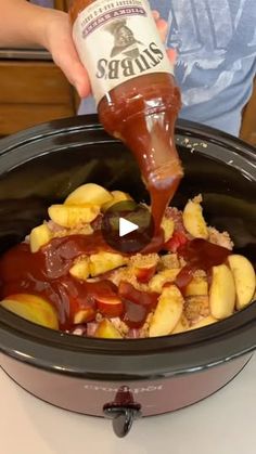 a person pouring sauce into a crock pot filled with food