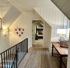 a hallway with white walls and wood flooring next to a wooden table in front of a stair case