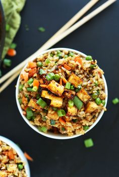 two bowls filled with rice and vegetables next to chopsticks on a black surface