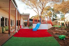 An outdoor childcare playground with a blue slide attached to a white platform with orange gates on fake grass. Close Proximity, Preschool Fun