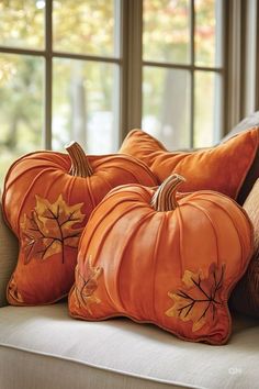 three decorative pumpkins sitting on a couch in front of a window with fall leaves