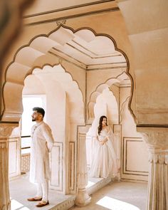 a man and woman dressed in white standing next to each other near an archway with arches