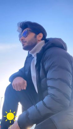 a man sitting on top of a wooden bench wearing sunglasses and a coat with the sun reflected in his eyes