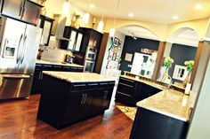 a large kitchen with stainless steel appliances and wood flooring, along with black cabinets