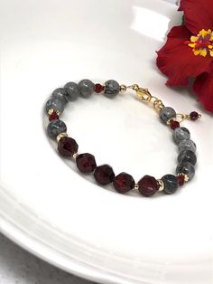 This gorgeous piece features deep, velvety red garnet surrounded by grey crazy lace agate. 14k gold filled beads are nestled throughout for extra sparkle. The contrast of the richly-hues garnet and swirled gray agate is simply exquisite! Finished with 14k gold filled chain and lobster claw clasp. A tiny garnet charm completes this glamorous bracelet. Choose from 3 adjustable sizes: Small (6.25 to 7 inches) Medium (7 to 8 inches) Large (8 to 9 inches) Elegant Gray Bracelets With Natural Stones, Elegant Gray Bracelets With Gemstone Beads, Elegant Gray Gemstone Beads Bracelets, Adjustable Red Agate Beaded Bracelets, Handmade Red Agate Bracelets, Elegant Garnet Gemstone Bracelets, Elegant Red Agate Bracelets, Red Agate Beaded Bracelet For Meditation, Gray Bracelet