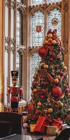 a decorated christmas tree in the middle of a room with large windows and decorations on it