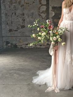 a woman in a white dress holding a bouquet of flowers next to a brick wall