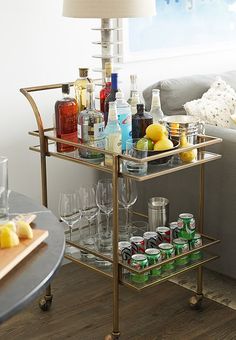 a bar cart filled with drinks on top of a wooden floor next to a couch