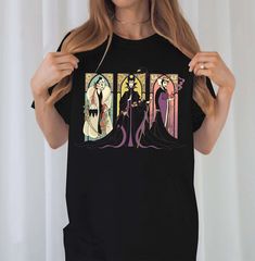 a woman holding up a black t - shirt with an image of maleficent and femaleficent on it