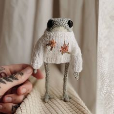 a small stuffed frog wearing a sweater with leaves on it's chest and eyes