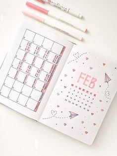 an open planner with pink markers and pencils next to it on a white surface