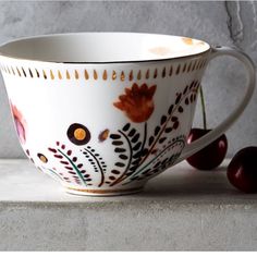 a white cup sitting on top of a counter next to two cherries