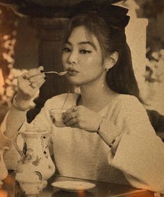 a woman sitting at a table eating food with chopsticks in her mouth and drinking from a cup