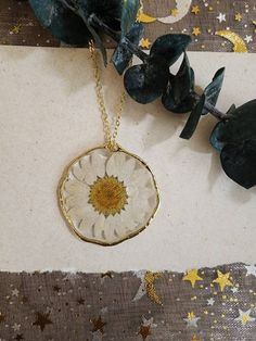 a white and gold necklace with a sunflower in the center on a brown background