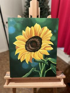 a sunflower painted on an easel in front of a christmas tree