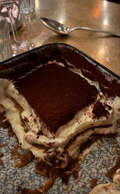 a chocolate dessert with white frosting on a blue and white plate next to utensils