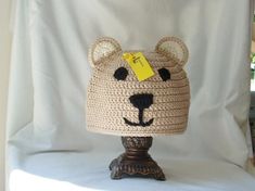 a crocheted bear hat sitting on top of a wooden stand next to a white curtain