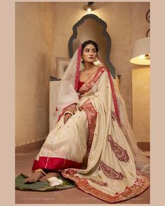 a woman sitting on the floor wearing a white and red sari