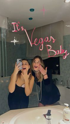 two women taking a selfie in front of a mirror with the words it's vegas baby written on it