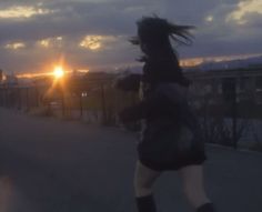 a woman is running down the street at sunset with her hair blowing in the wind