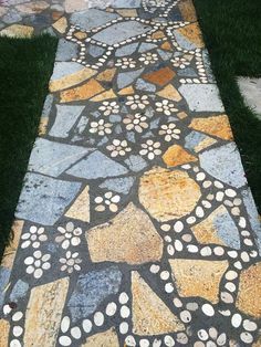 a walkway made out of stones with flowers on the side and grass in the background