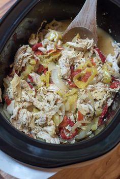 a slow cooker filled with chicken, peppers and onions next to a wooden spoon