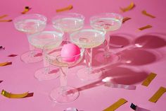 several wine glasses filled with pink and yellow liquid next to confetti streamers