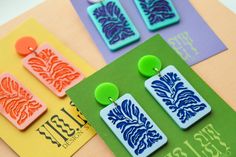 three pairs of colorful earrings sitting on top of a table next to cards and envelopes