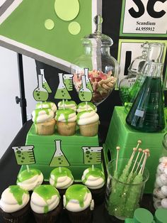 green and white cupcakes are on display in front of the science themed dessert table