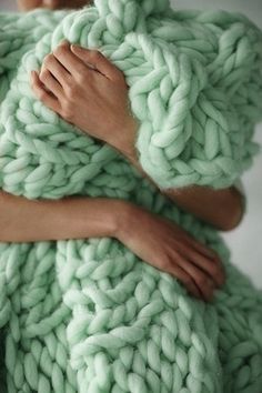 a woman is wrapped up in a giant chunky blanket, with her hands on the back