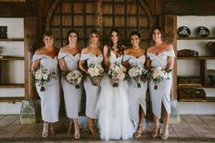 a group of women standing next to each other in front of a wooden wall holding bouquets