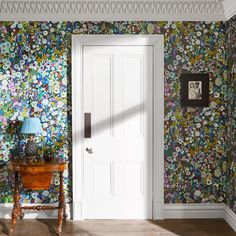 a room with wallpaper and a table in the corner next to a door that has a lamp on it