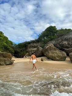 a man in white trunks walking into the water on a beach next to large rocks