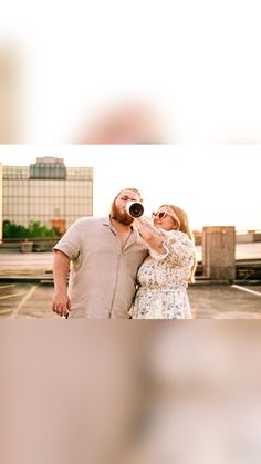 a man and woman standing next to each other drinking out of beer bottles in front of buildings