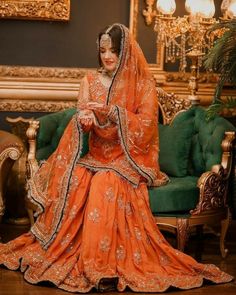 a woman in an orange bridal gown sitting on a green couch wearing a veil