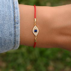 "The tradition of red string bracelets dates back many hundreds of years. The red color is meant to symbolize Protection and Good Luck. Paired with a beautifully crafted evil eye, this bracelet is sure to bring good vibes and protection to its owner ✨ ➤Details➤ ▪︎ Made of 925 Sterling Silver ▪︎ Plated in 14k Gold or Rhodium ▪︎ Durable, High Quality Red String ▪︎ Measures 6.75\" + 1.5\" Extension Chain ▪︎ Lobster Clasp Closure ▪︎ Evil Eye Charm features a vibrant, sapphire cz stone in the center Red Beaded Bracelets As Festival Gift, Traditional Red Wristband As Gift, Traditional Red Braided Bracelets As Gift, Traditional Red Braided Bracelets For Gift, Traditional Red Wristband Gift, Traditional Red Wristband For Gift, Red Spiritual Bracelets For Friendship, Red Adjustable Bracelets For Festivals, Adjustable Red Jewelry For Festivals