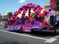 a parade float with people riding in it's back and balloons on the side