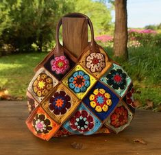 a multicolored crocheted purse sitting on top of a wooden table next to a tree